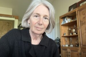A woman with gray hair is sitting in front of a bookshelf.